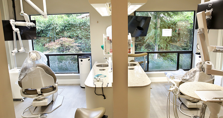A direct view into two patient rooms shows a clean, empty room featuring a patient chair, countertop, and service tray.