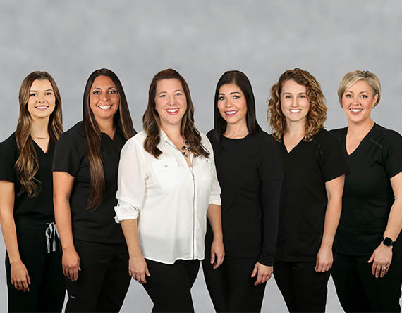 The five female employees at Ashley Harrison DDS standing in a line, smiling.