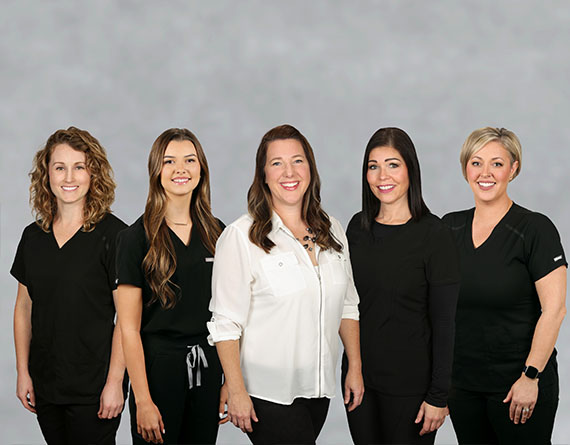 The five female employees at Ashley Harrison DDS standing in a line, smiling.