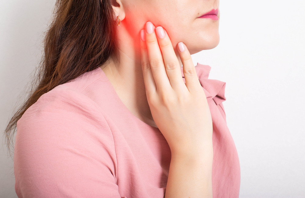 Woman holding her jaw and neck with red highlight indicating tooth pain and infection before treatment.