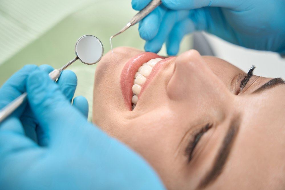 Dentist performing a professional dental exam using a mirror and scaler to check for cavities, stains, and overall oral health